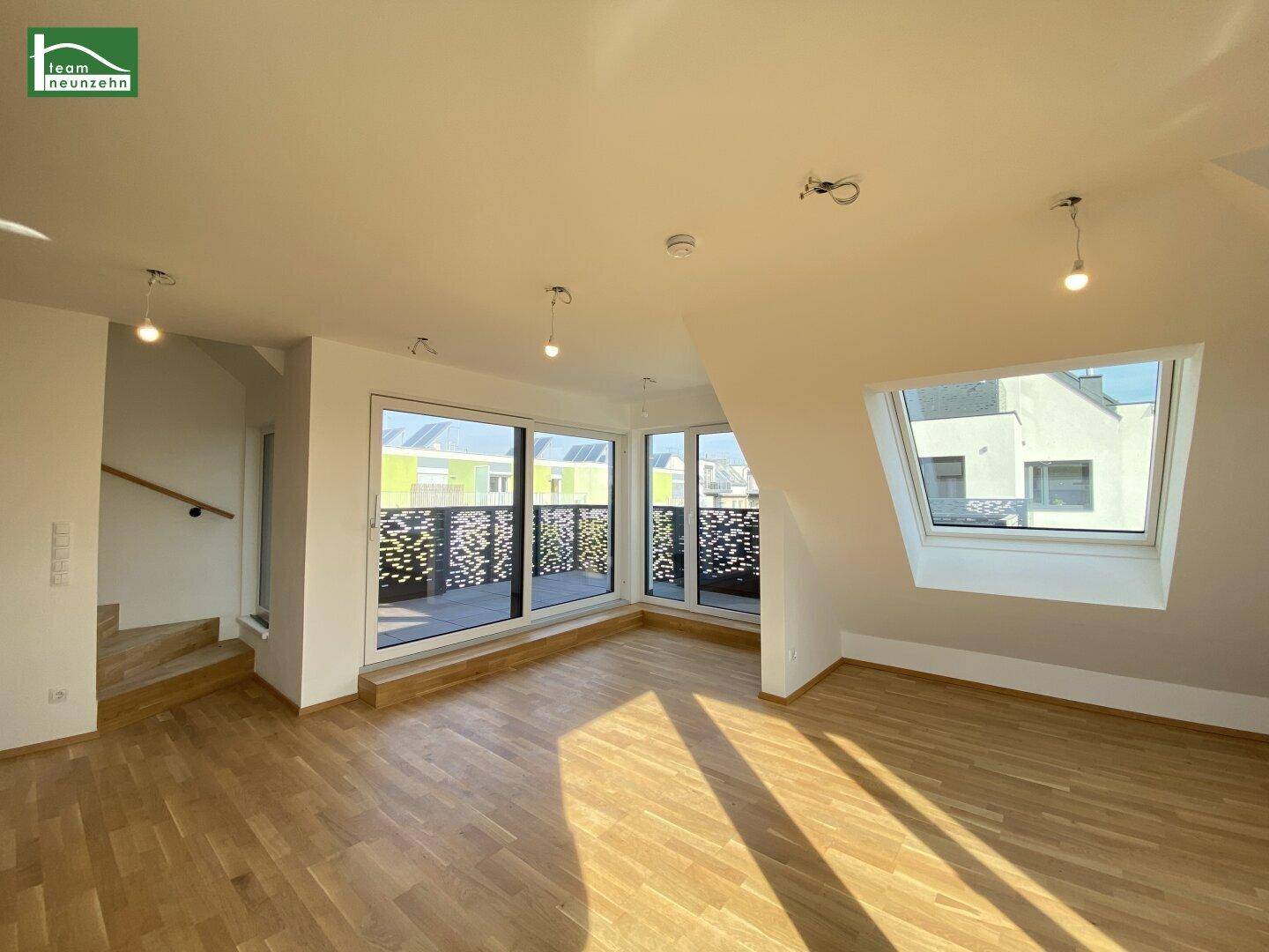Geräumiges Wohnzimmer mit Parkettboden, großen Fenstern, Dachschräge und Zugang zu einem Außenbereich.