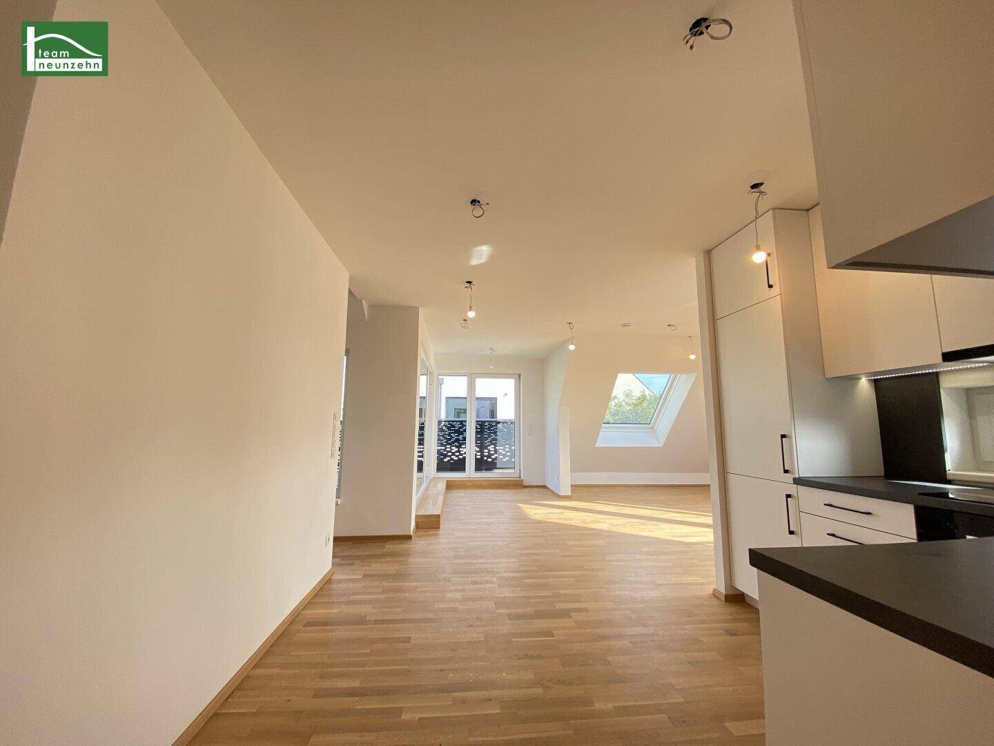 Heller offener Wohnbereich mit Holzparkett und integrierter Küche, lichtdurchflutet durch große Fenster.
