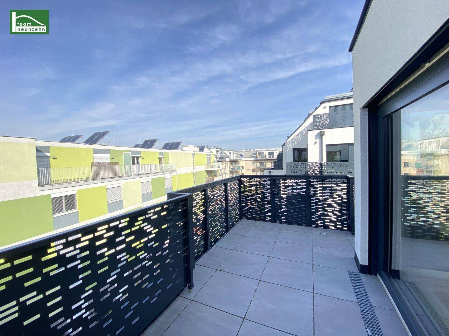 Moderner Balkon mit Lochblechgeländer und Blick auf benachbarte Gebäude mit Solaranlagen.