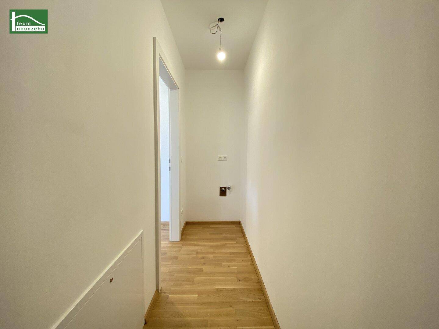Heller Flur mit Parkettboden und weißen Wänden, führt zu weiteren Räumen.