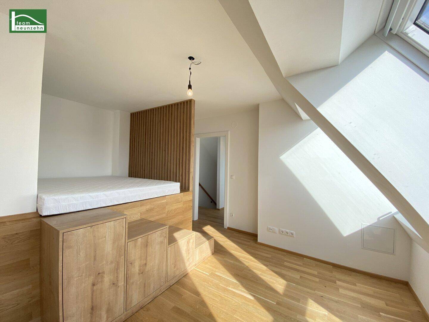 Modernes Schlafzimmer im Dachgeschoss mit erhöhtem Bettpodest und Holzvertäfelung.