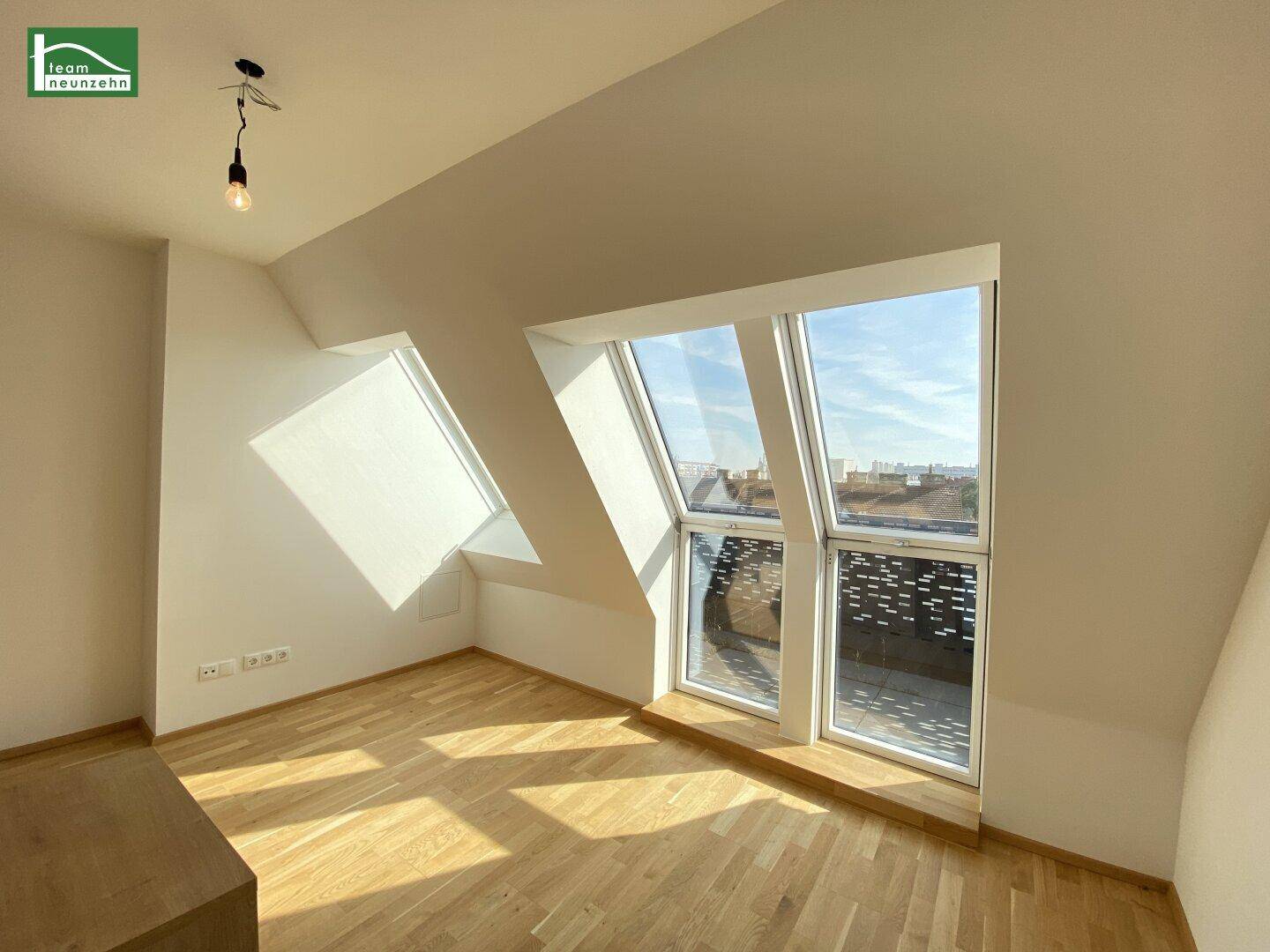 Helles Zimmer im Dachgeschoss mit Holzparkett und großen Dachfenstern, die viel Licht hereinlassen.