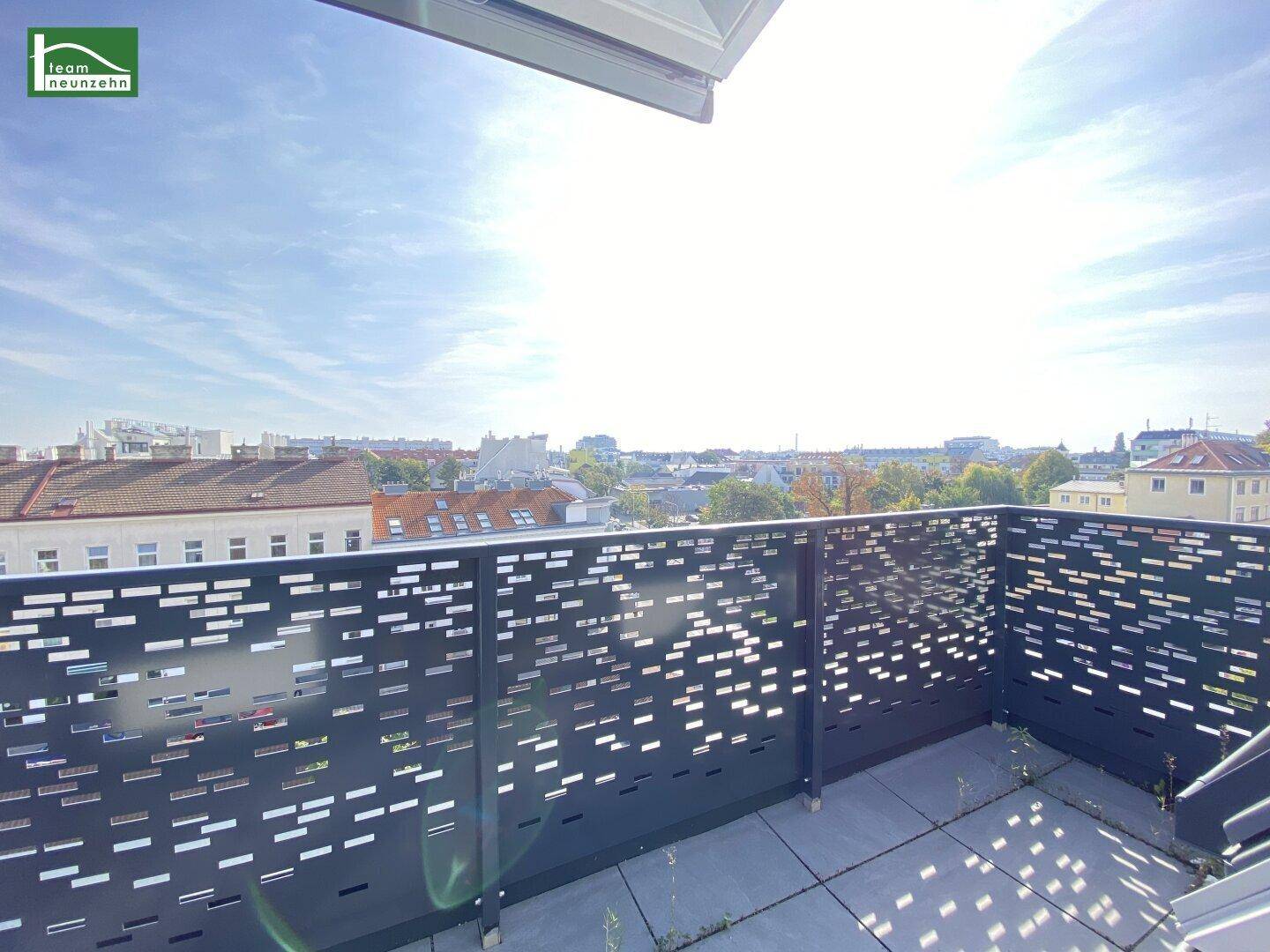 Heller Balkon mit perforiertem Geländer und weitem Blick über die Stadtlandschaft bei Sonnenschein.