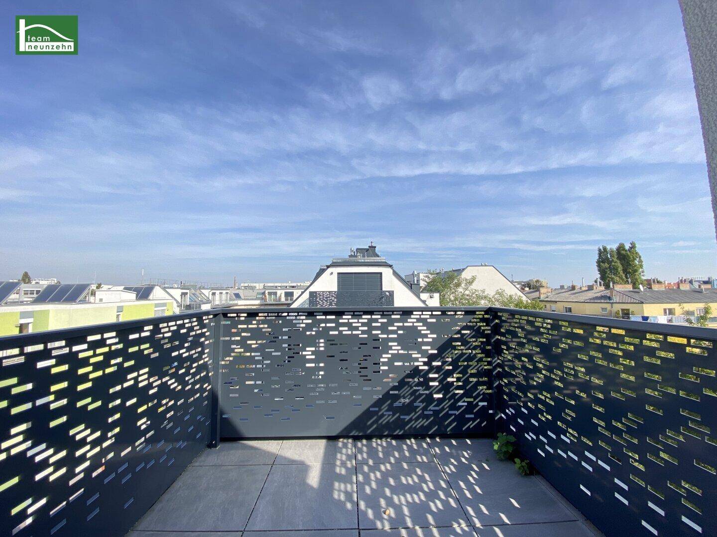 Geräumiger Balkon mit modernem Lochblechgeländer und Blick auf die umliegenden Dächer.