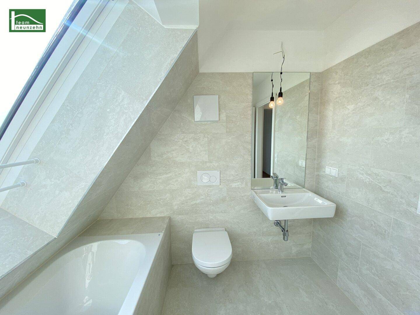 Helles Badezimmer im Dachgeschoss mit Badewanne, Wand-WC und modernem Waschtisch.