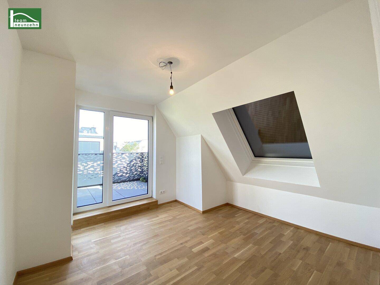 Helles Schlafzimmer im Dachgeschoss mit Holzparkett und Zugang zu einem Balkon.