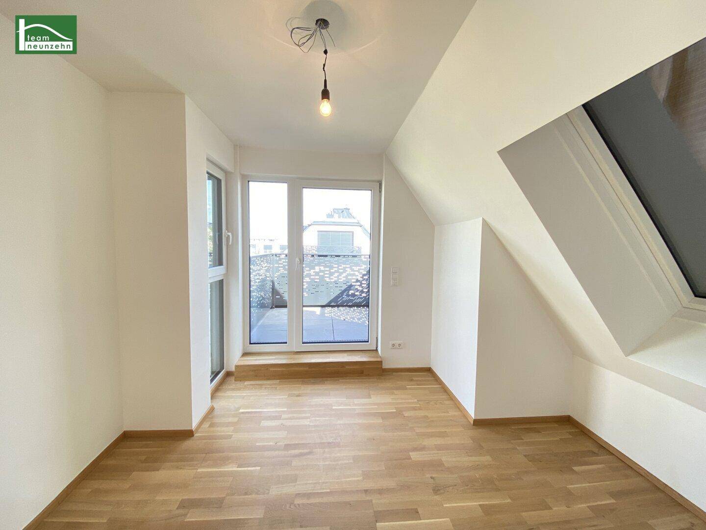 Lichtdurchflutetes Schlafzimmer im Dachgeschoss mit Holzparkett und Zugang zu einem Balkon.