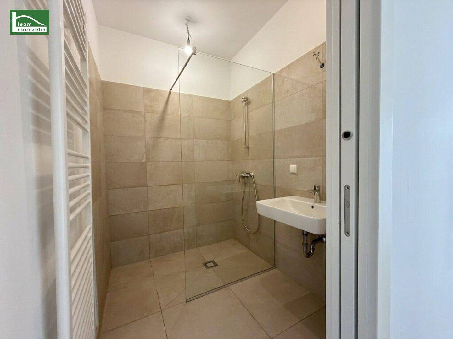 Modernes Badezimmer mit beigefarbenen Fliesen, ebenerdiger Dusche und Handtuchheizkörper.