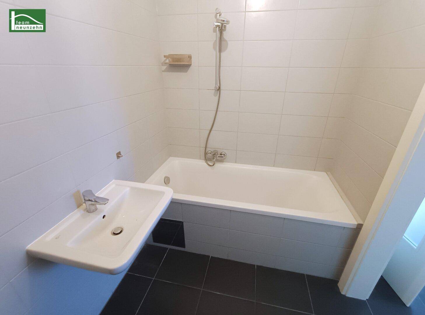 Funktionales Badezimmer mit Badewanne, Waschbecken und weißen Fliesen an den Wänden.
