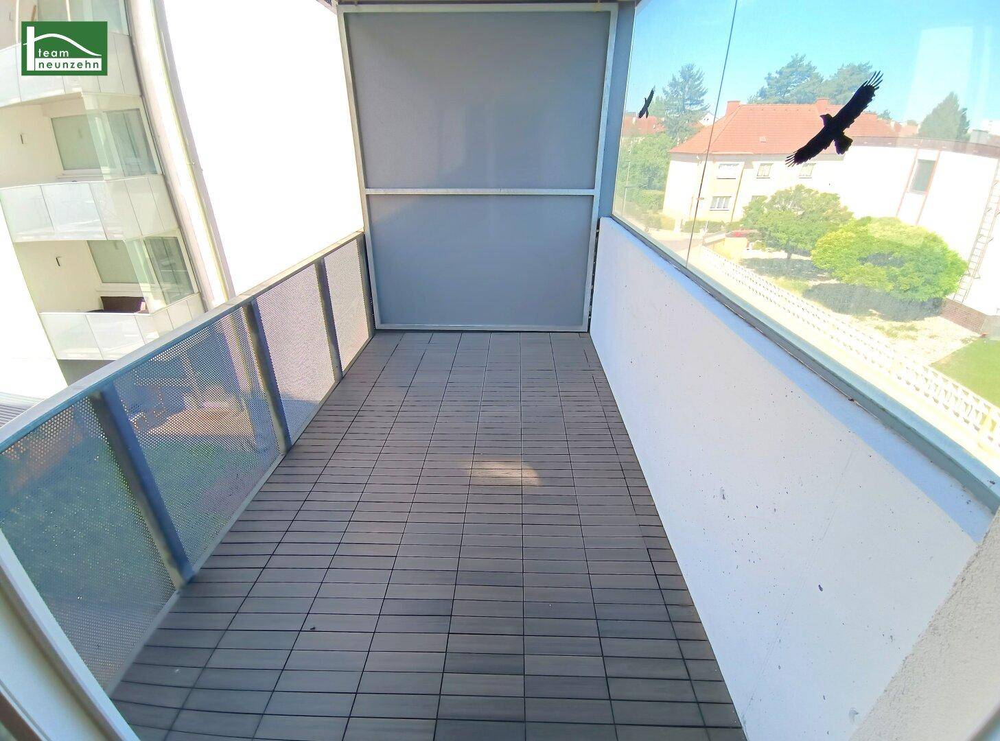 Geräumiger Balkon mit Fliesenboden und Glasbrüstung, bietet einen Blick auf die Umgebung.