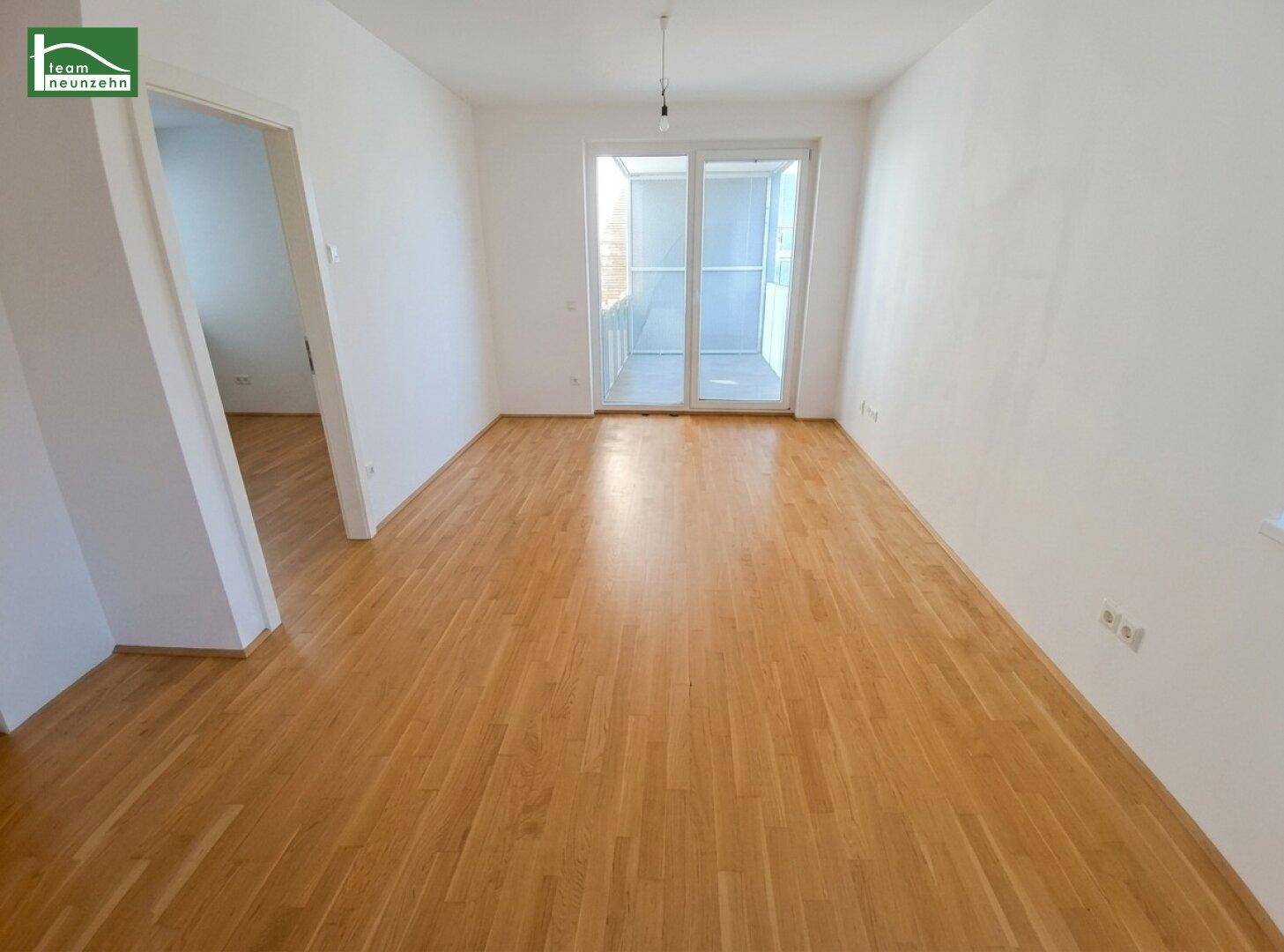 Geräumiges, unmöbliertes Wohnzimmer mit hellem Parkettboden und Zugang zum Balkon.