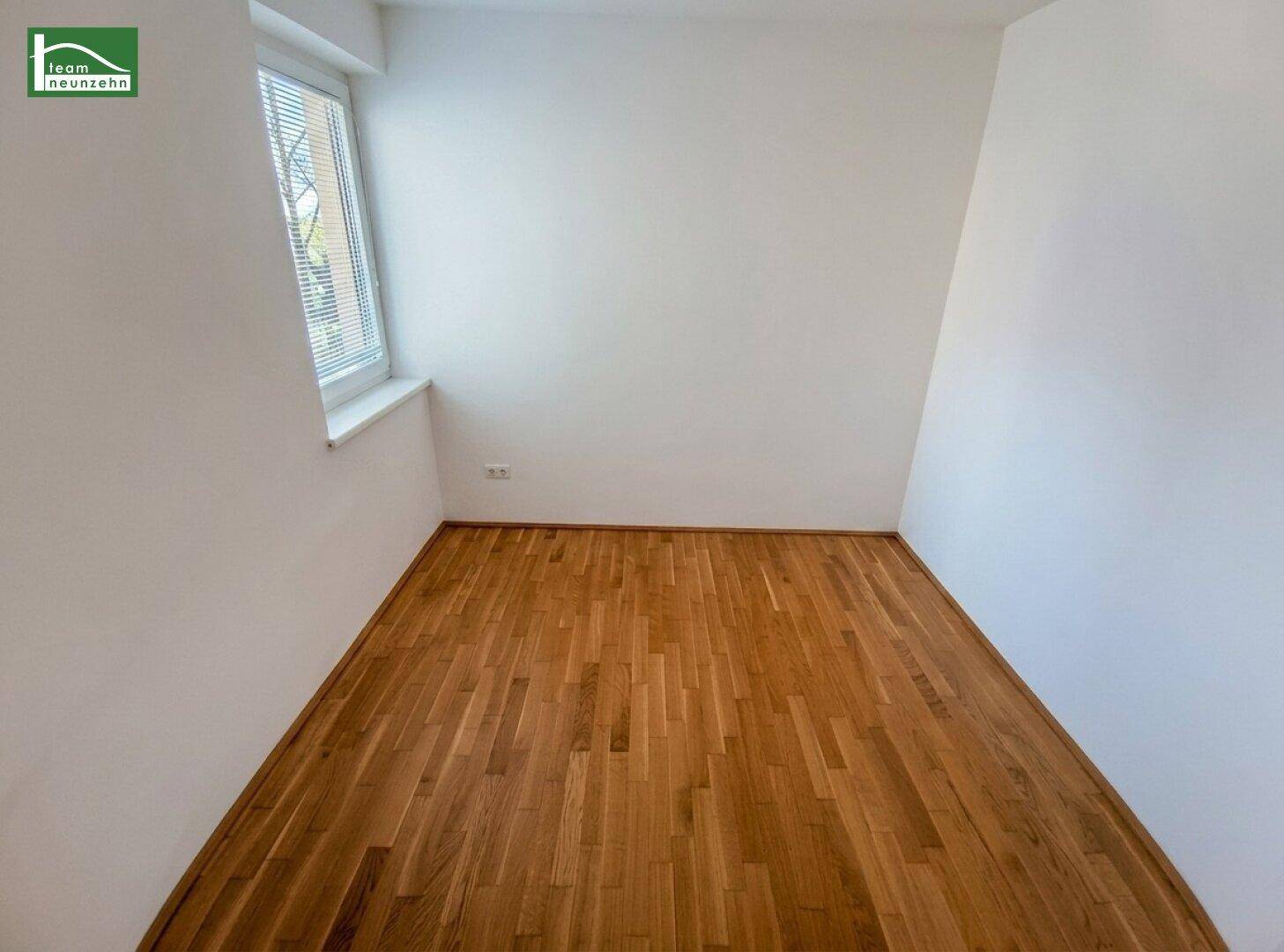 Helles Schlafzimmer mit Parkettboden und Fenster, das viel Tageslicht hereinlässt.
