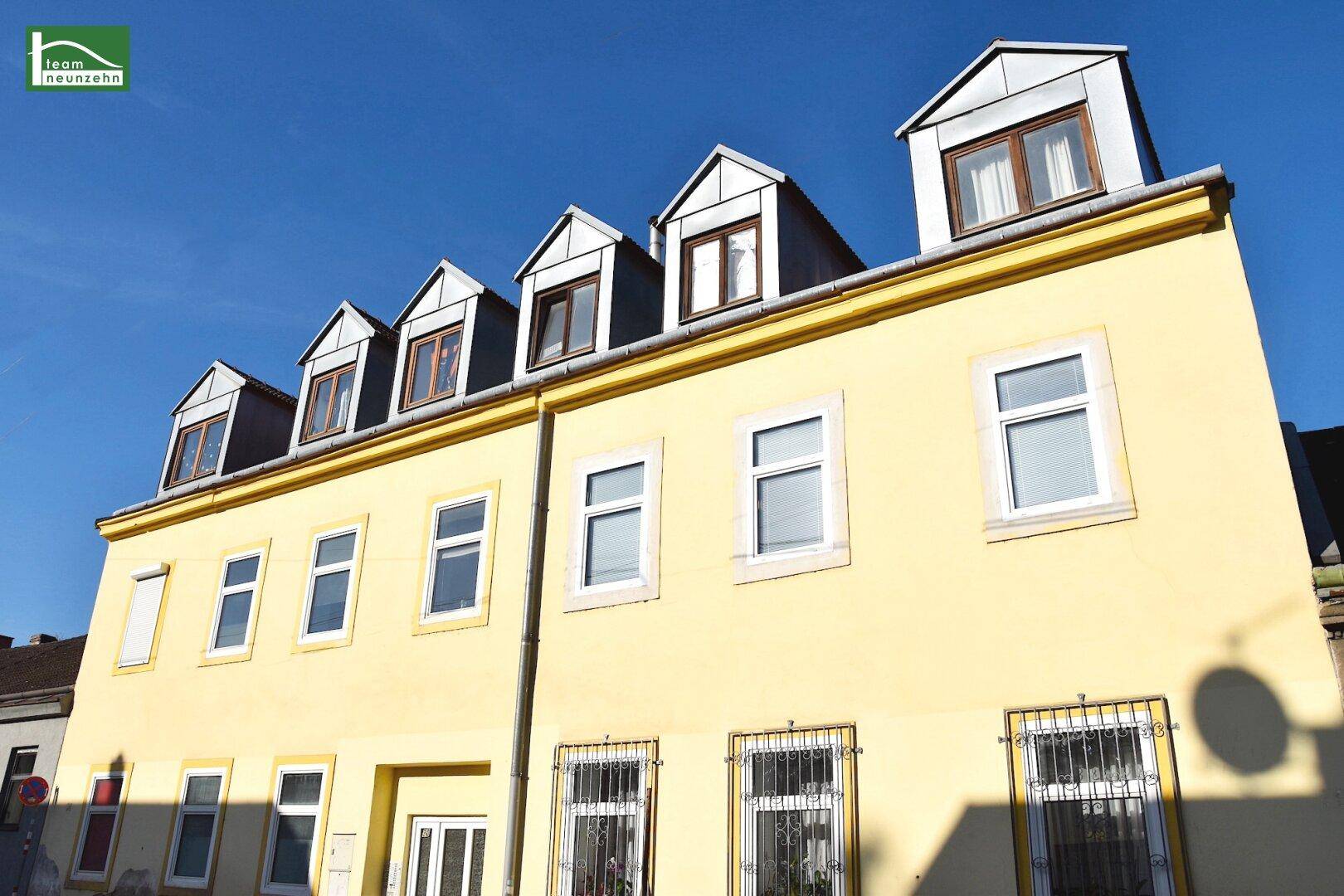 Gelbe Fassade eines Altbaus mit mehreren Gaubenfenstern unter strahlend blauem Himmel.