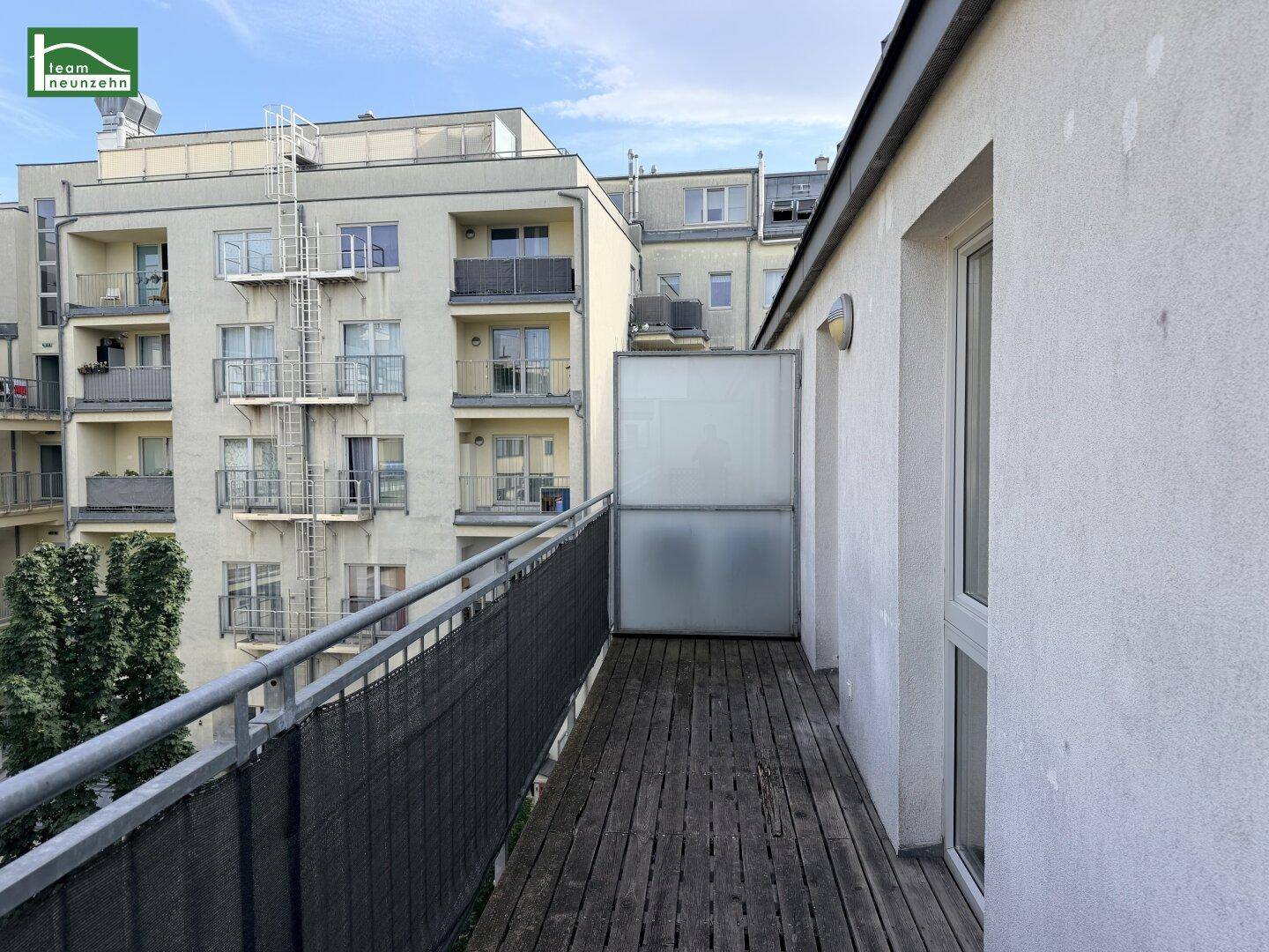 Langer Balkon mit Holzboden und Blick auf die umliegenden Wohngebäude.