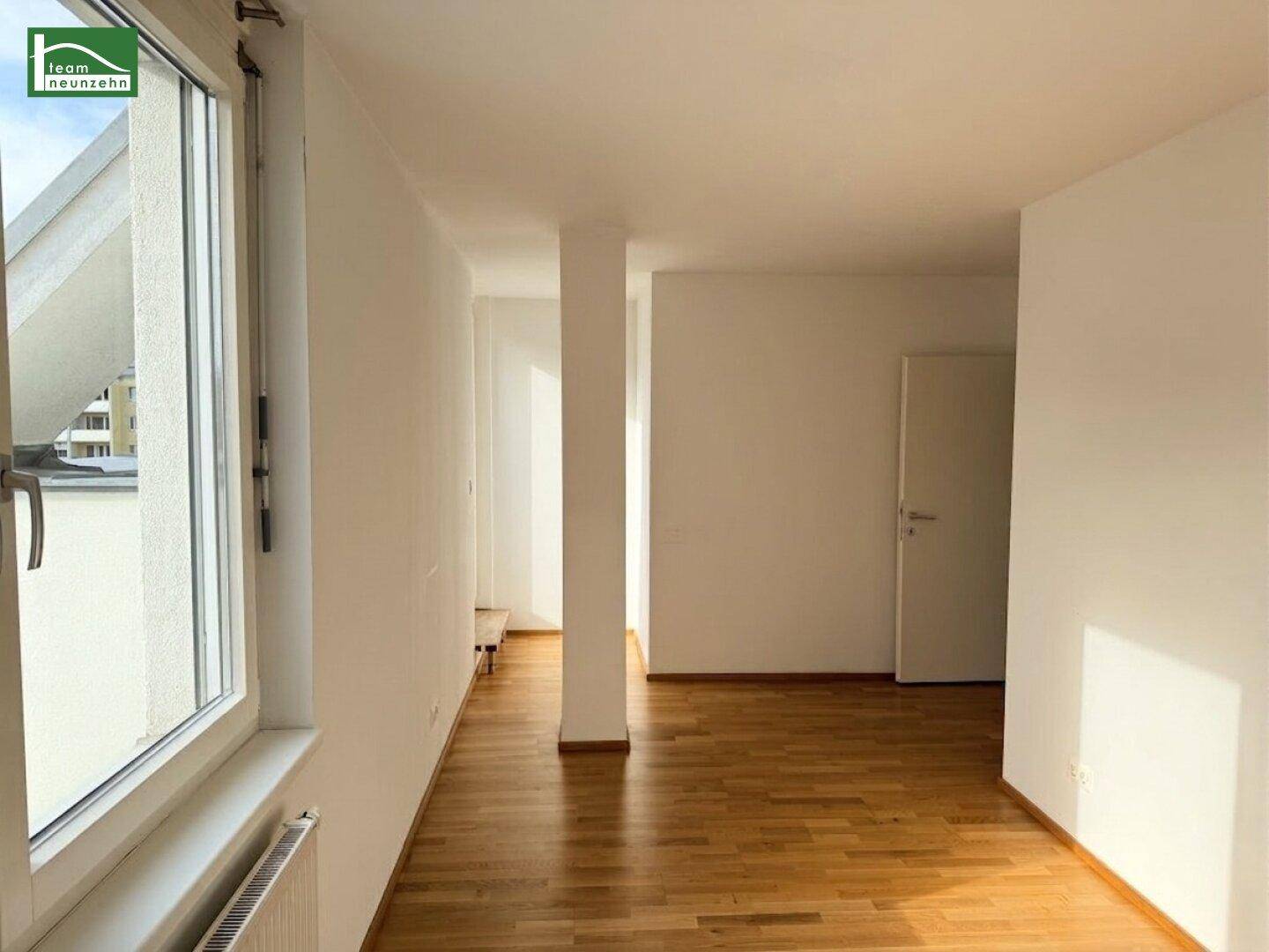 Heller, offener Raum mit Holzboden und einer tragenden Säule, ideal für flexible Nutzung.