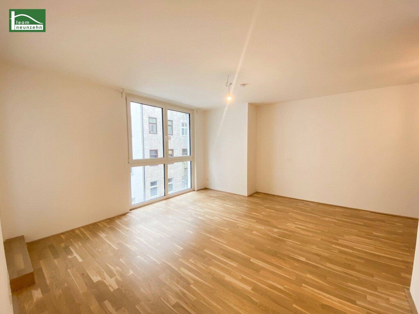 Geräumiges Wohnzimmer mit großen Fenstern, die viel Tageslicht hereinlassen und Parkettboden.