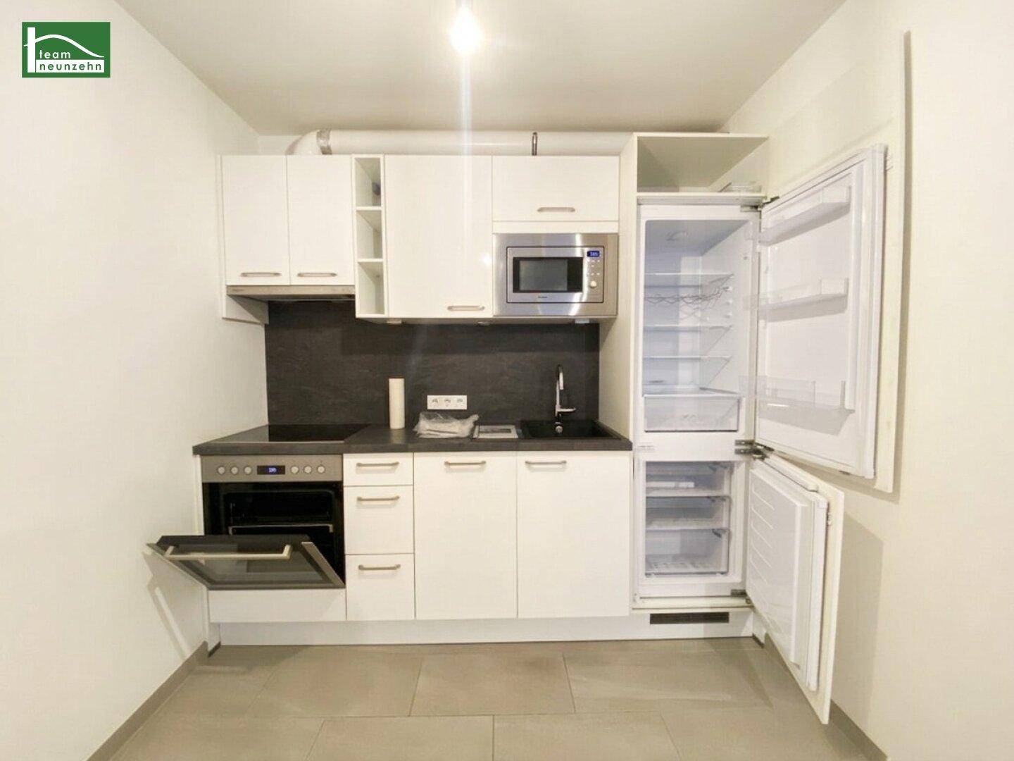 Moderne Küchenzeile mit weißen Schränken, integrierten Geräten und einem Kühlschrank.