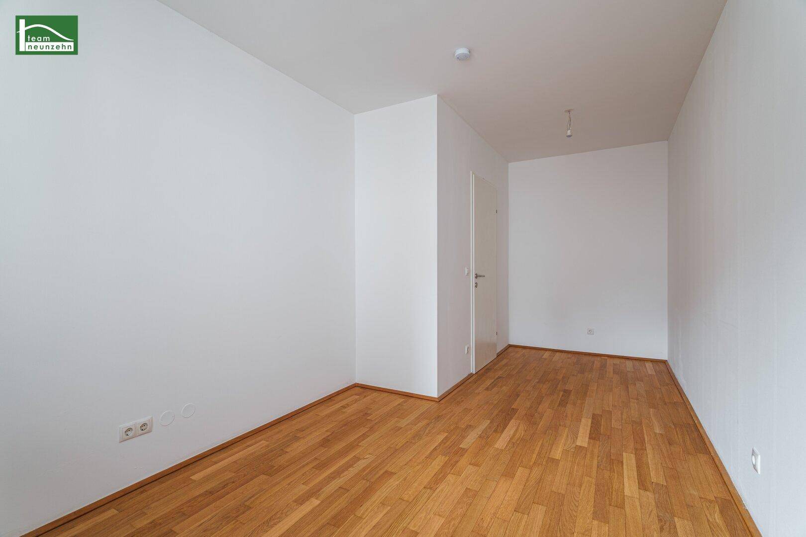 Geräumiges, leeres Zimmer mit Parkettboden und weiß gestrichenen Wänden, vielseitig nutzbar.