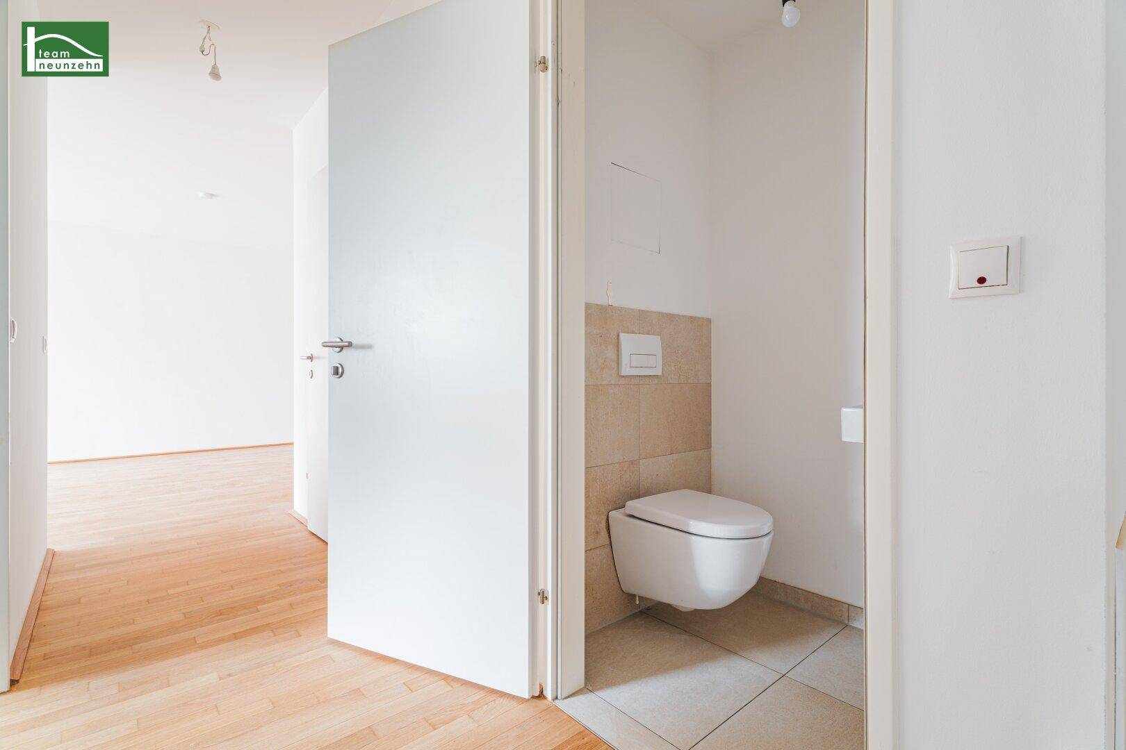 Separates Gäste-WC mit wandhängender Toilette und teilweiser Fliesenverkleidung.