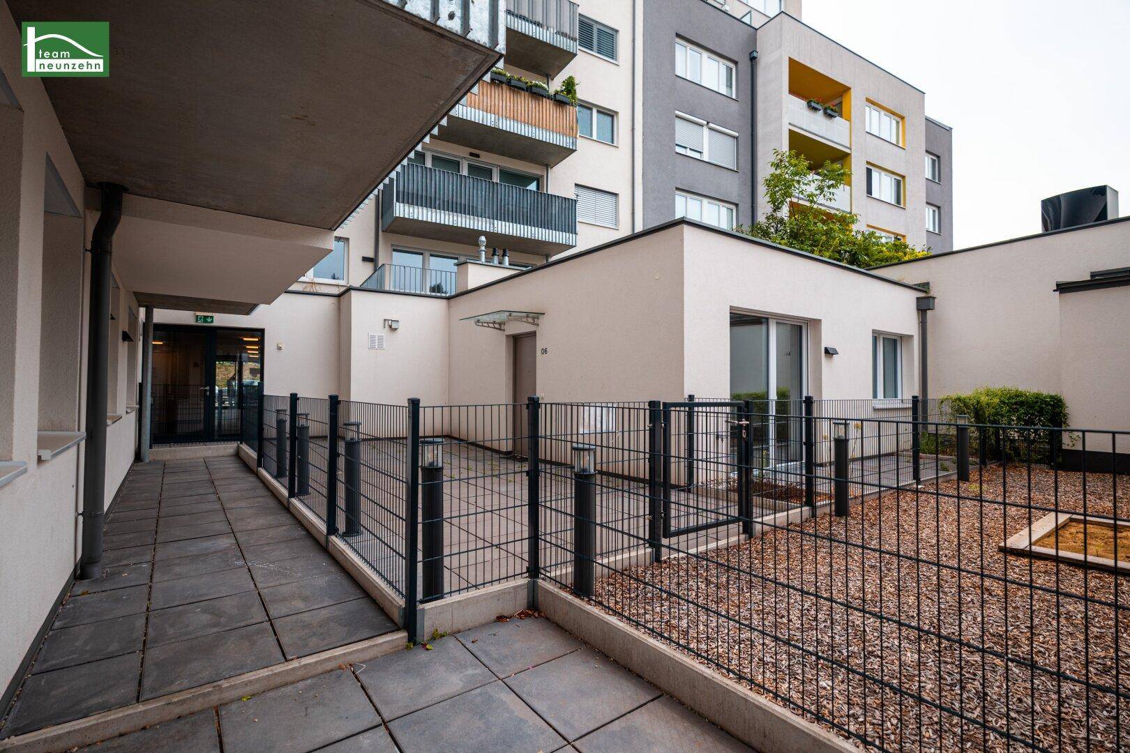 Große, gepflasterte Terrasse im Erdgeschoss mit Zaun und Blick auf das moderne Gebäude.