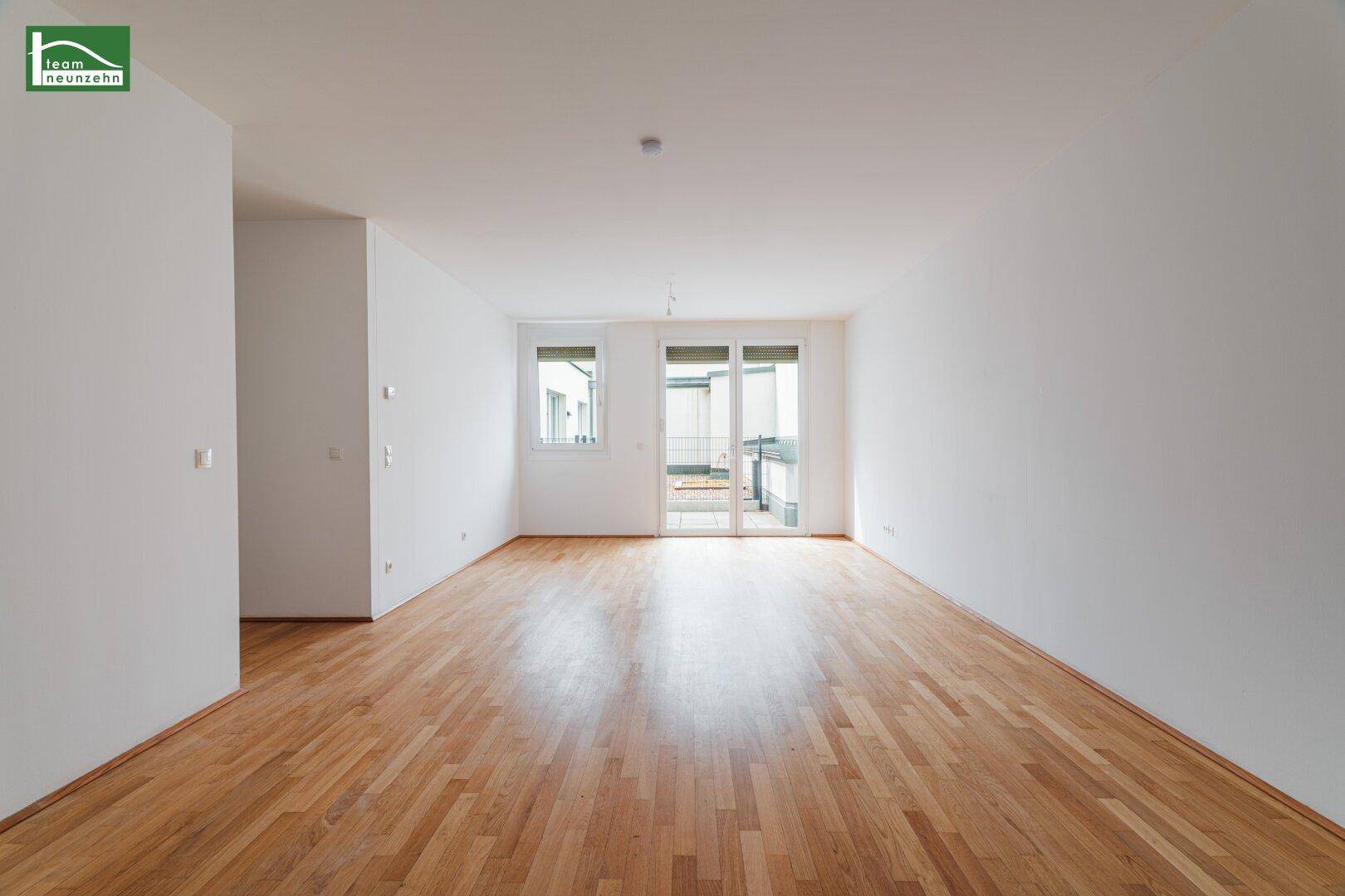 Heller Wohnbereich mit Holzparkettboden und Zugang zu einem Balkon oder einer Terrasse.