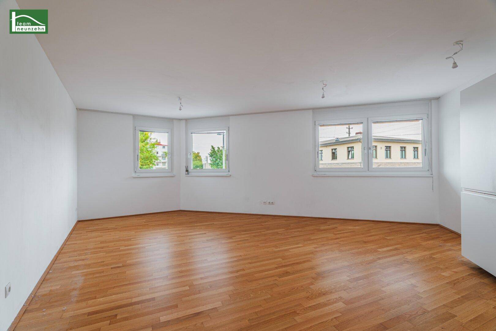 Geräumiges Wohnzimmer mit hellem Parkettboden und mehreren Fenstern für viel Tageslicht.