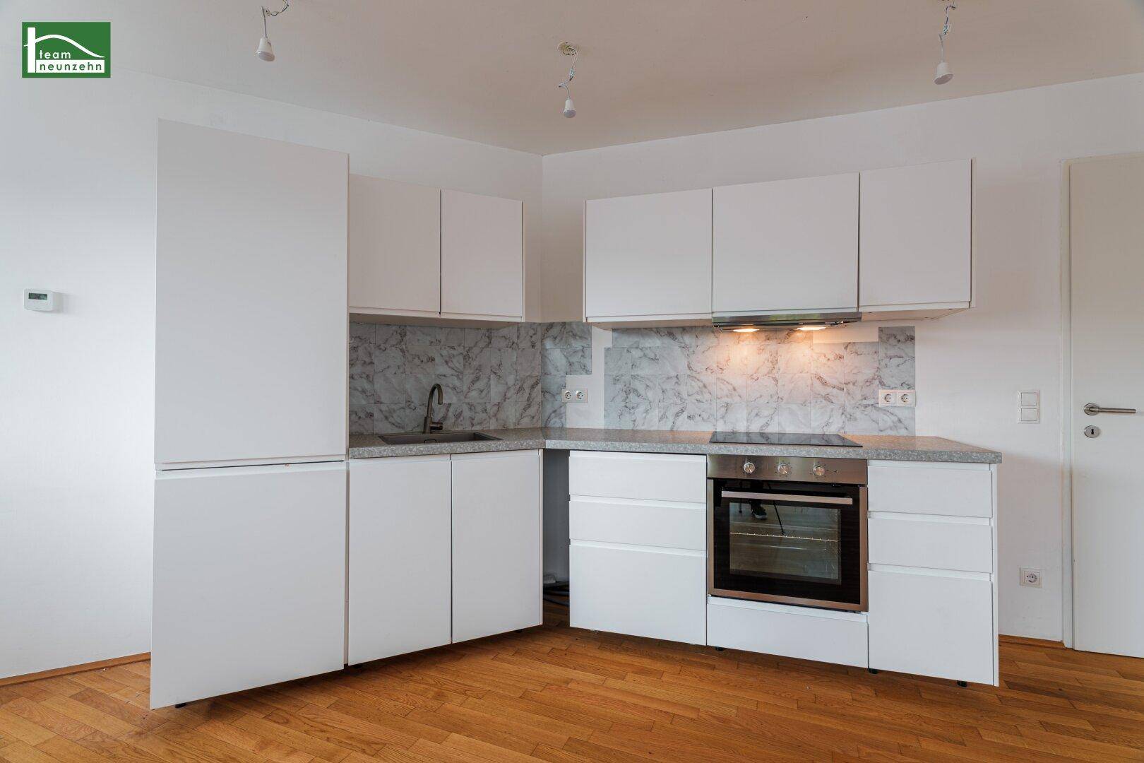 Moderne Einbauküche mit weißen Schränken, integrierten Geräten und Marmor-Optik-Rückwand.