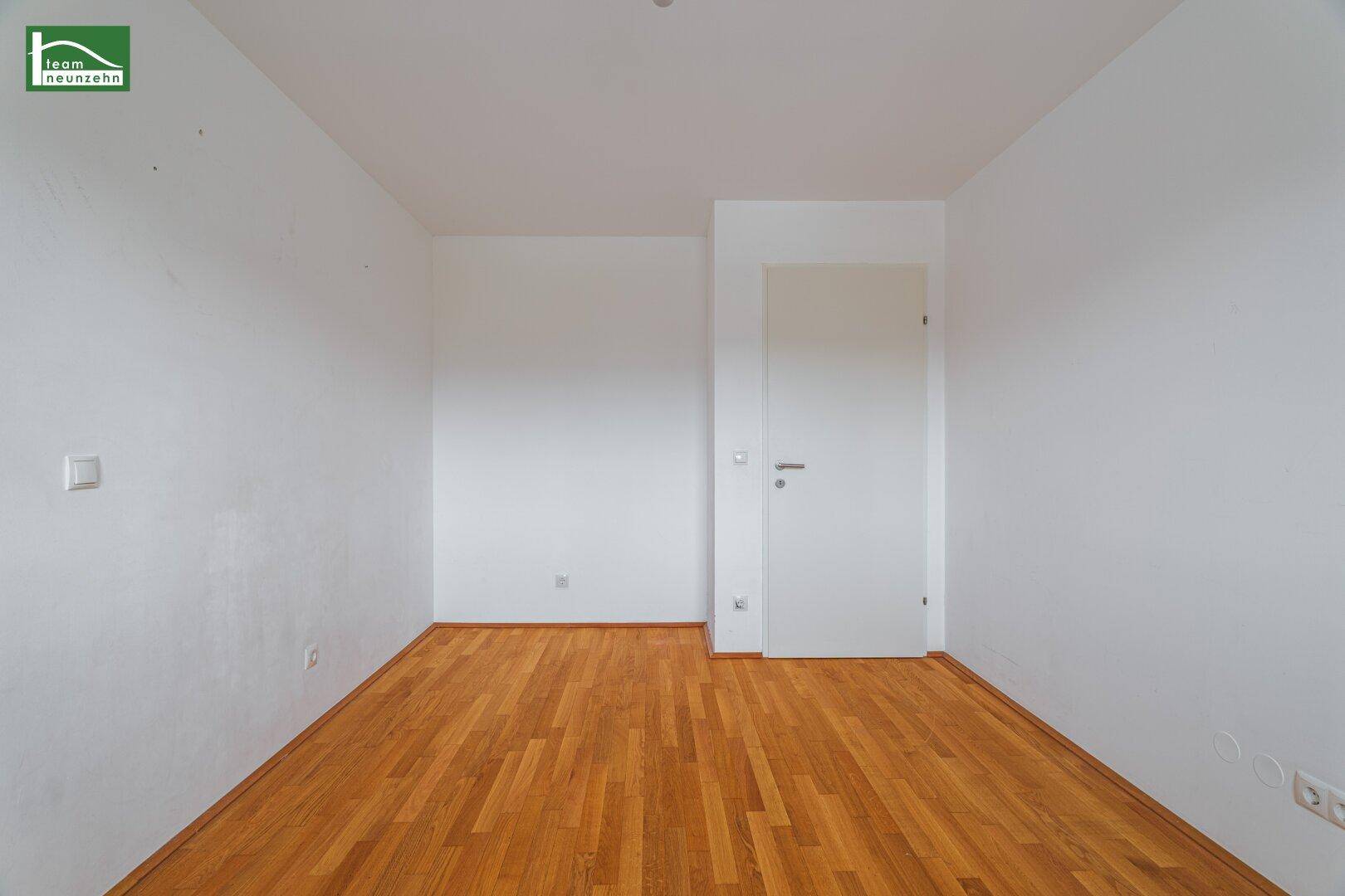 Leerer Raum mit Parkettboden und einer weißen Tür, bereit zur individuellen Gestaltung.