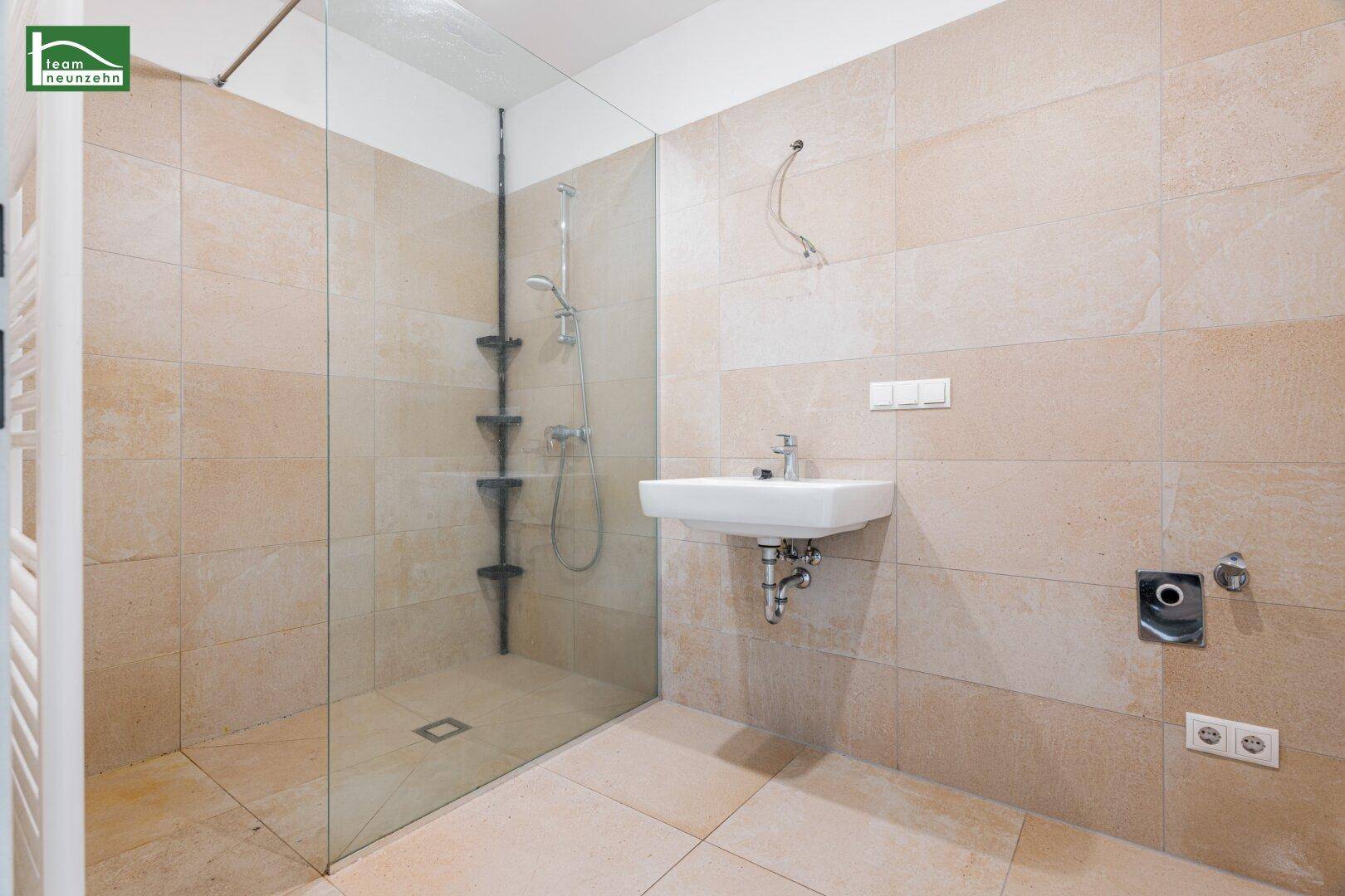 Modernes Badezimmer mit ebenerdiger Dusche, Glaswand und beigefarbenen Fliesen.