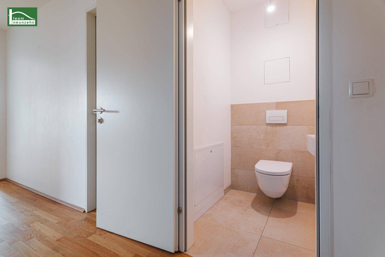 Modernes Gäste-WC mit wandhängendem WC, kleinem Waschbecken und beigefarbenen Fliesen.