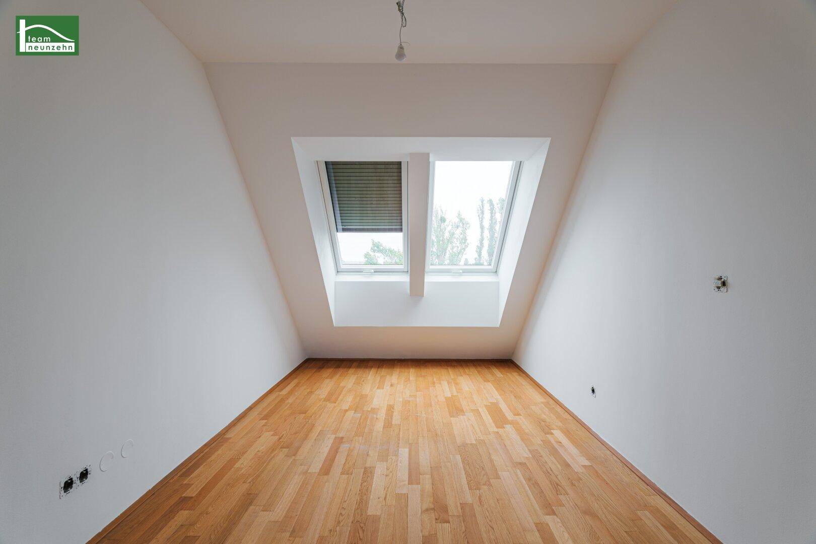 Helles Schlafzimmer mit Holzboden, weißen Wänden und zwei Dachfenstern, die viel natürliches Licht spenden.