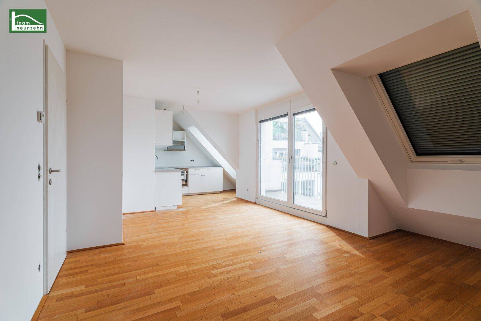 Offener Wohnbereich mit integrierter Küchenzeile, Holzfußboden und Zugang zu einem Balkon.