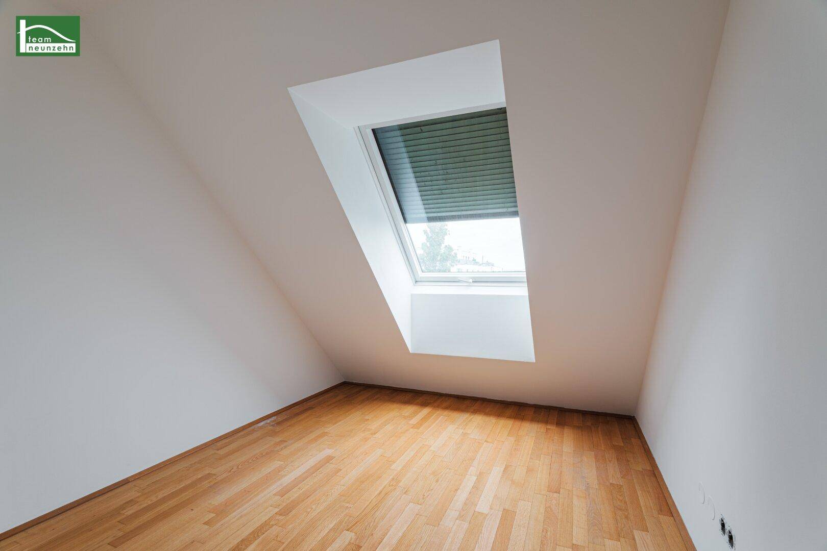 Ruhiges Schlafzimmer mit Holzboden, weißen Wänden und einem einzelnen Dachfenster für angenehmes Licht.