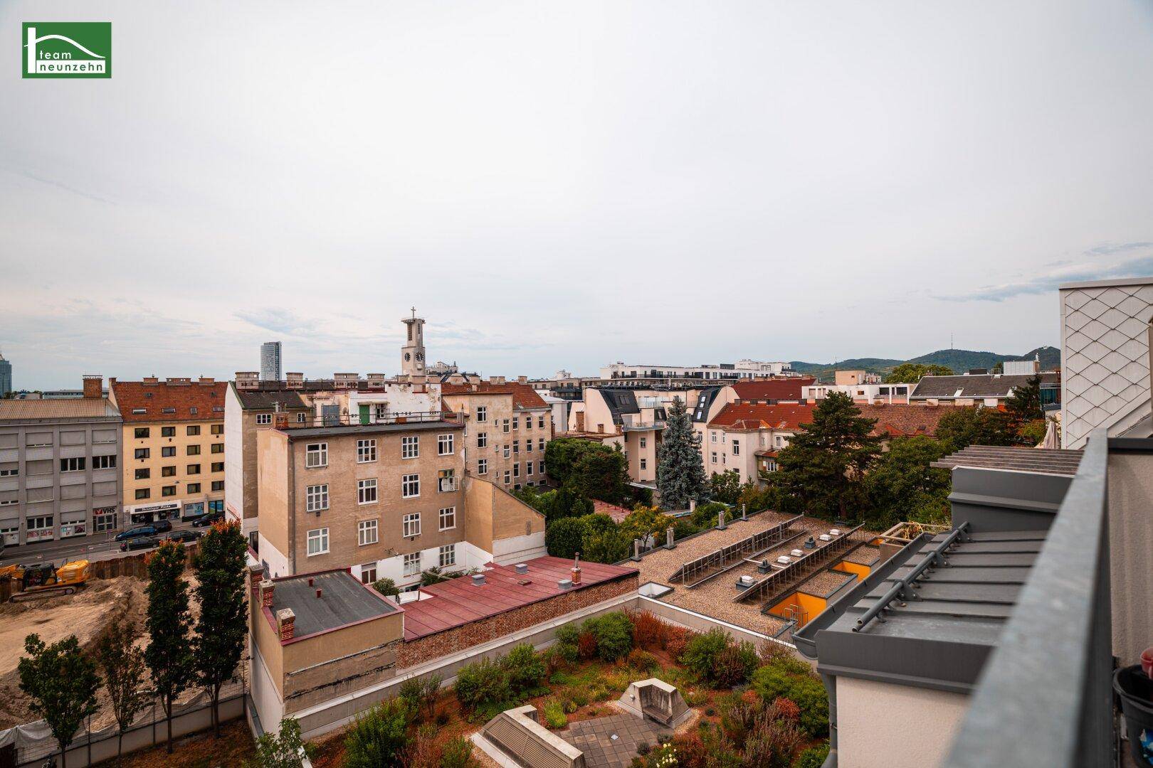 Weitläufiger Stadtblick von einem Balkon, der verschiedene Gebäude, Dächer und Grünflächen umfasst.