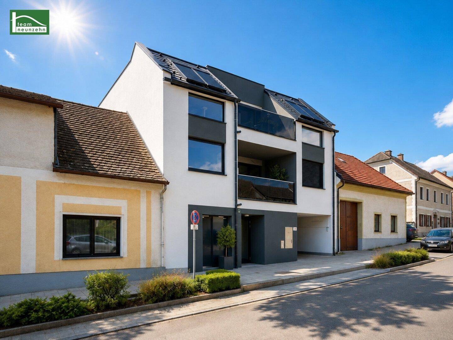 Moderne Wohnfassade mit Balkonen und Solaranlage auf dem Dach an einer sonnigen Straße.