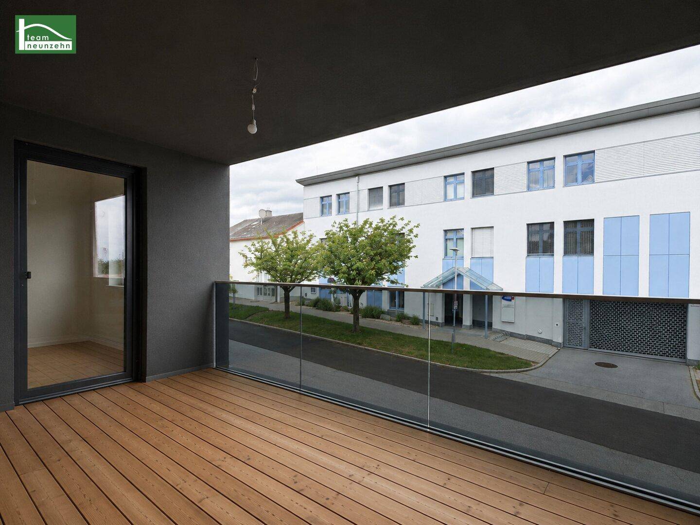 Moderner Balkon mit Holzbelag und Glasgeländer, bietet Blick auf die Umgebung.