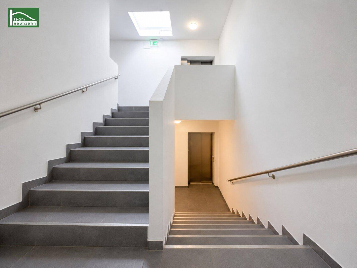 Helles Treppenhaus mit Fliesenstufen, Handläufen und einem Oberlicht für natürliches Licht.