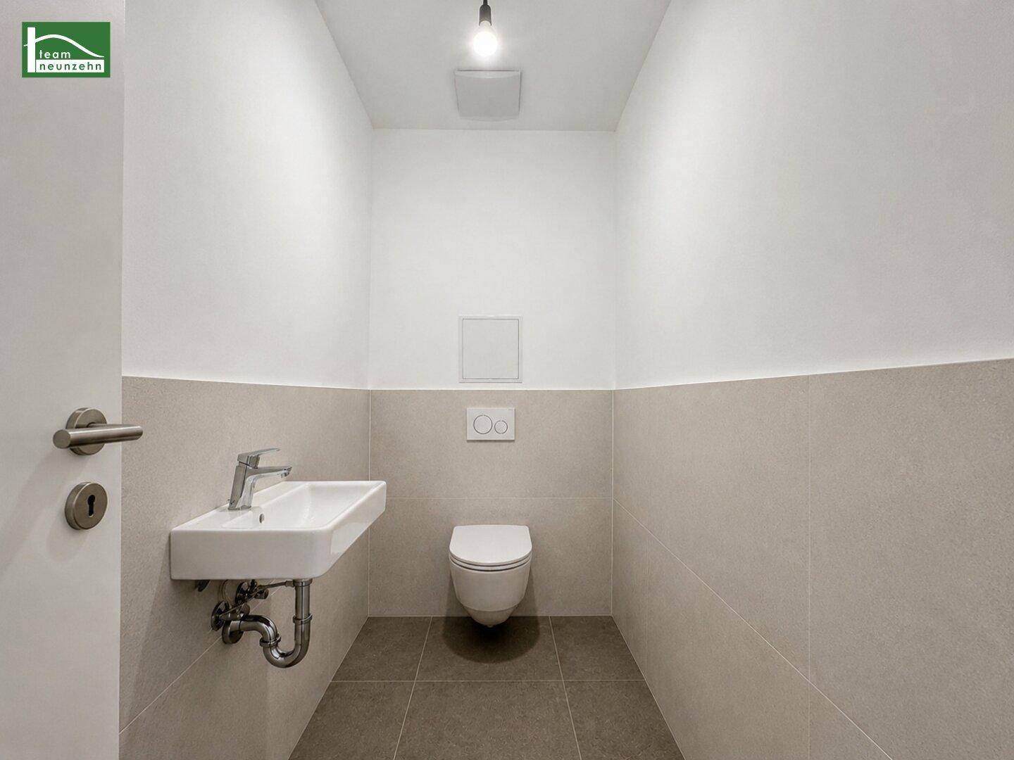 Leeres Gäste-WC mit wandhängender Toilette und vorbereiteten Anschlüssen für ein Waschbecken.