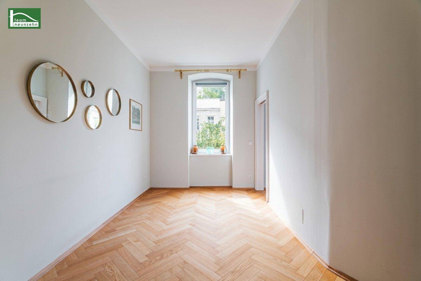Helles Zimmer mit Fischgrätparkett und einem Fenster, dekoriert mit runden Spiegeln.