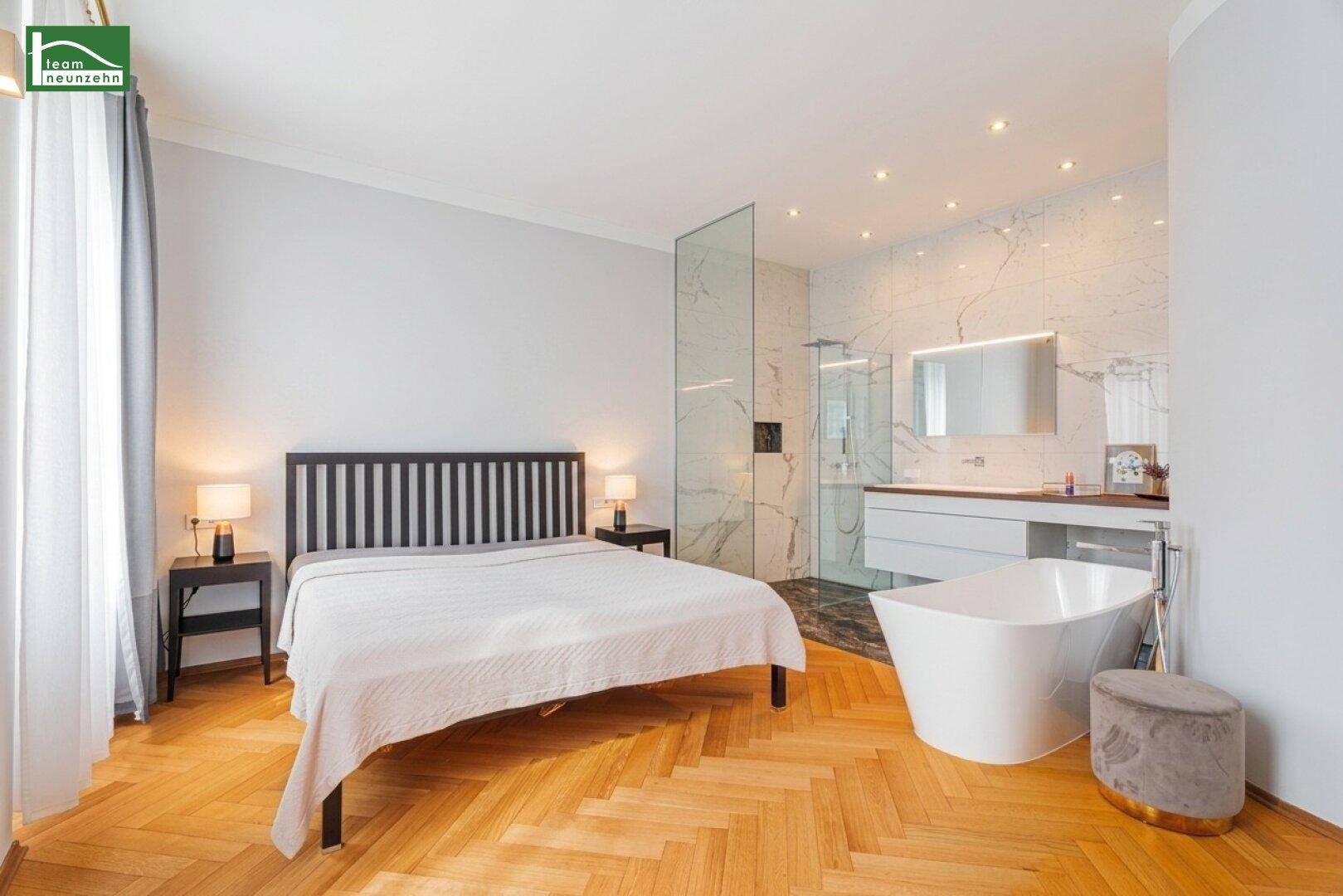 Schlafzimmer mit integriertem Badbereich, freistehender Badewanne und Marmorfliesen.