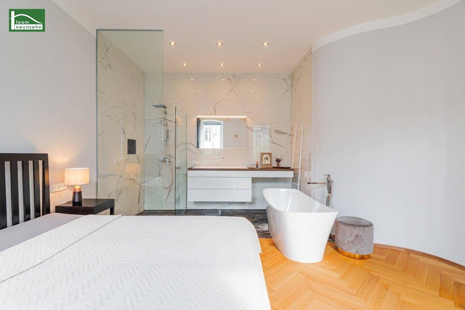 Elegantes Schlafzimmer mit offenem Badbereich, freistehender Wanne und Marmorwaschtisch.