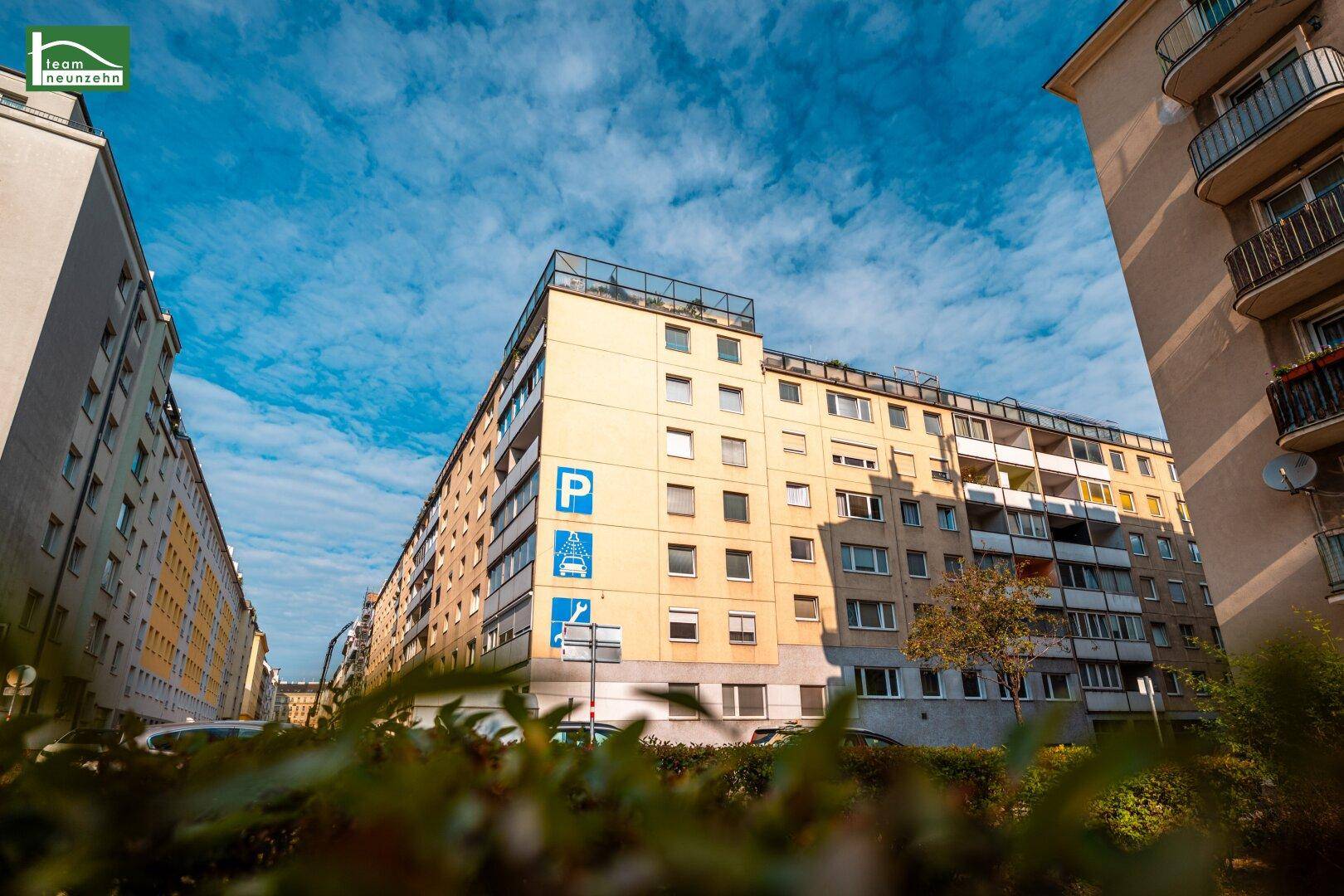 Außenansicht eines Wohngebäudes mit Parkplatzschild und blauem Himmel.