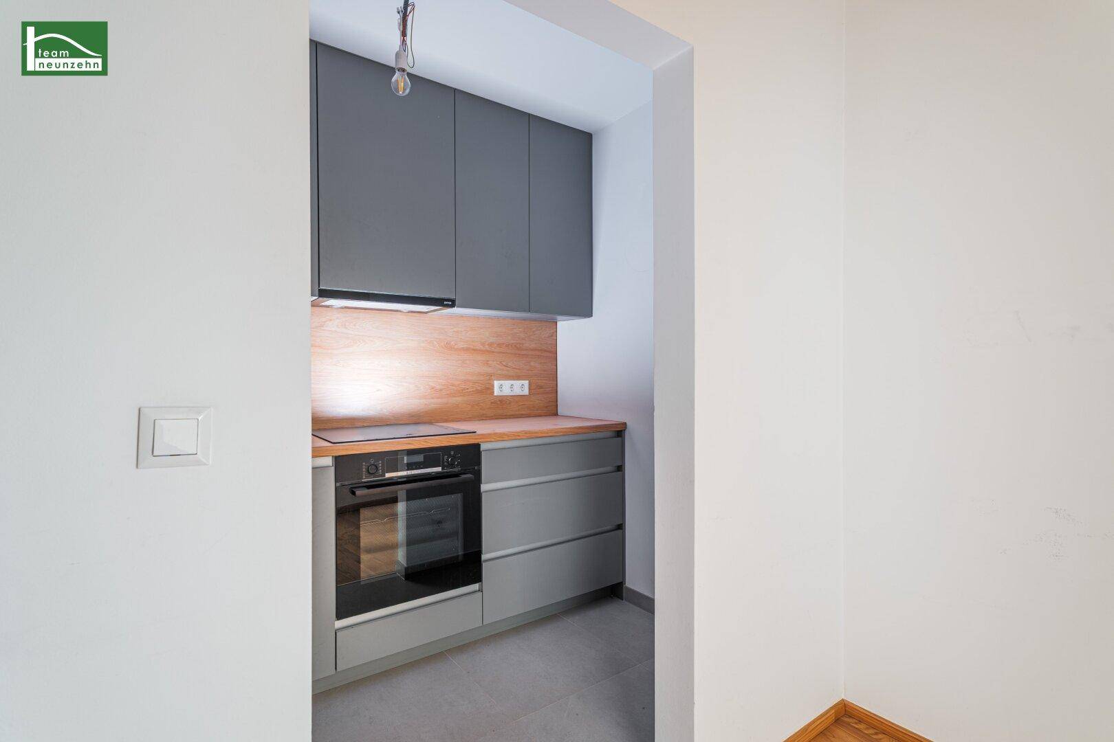 Detailansicht der Küchenzeile mit Kochfeld, Backofen und Holzrückwand.