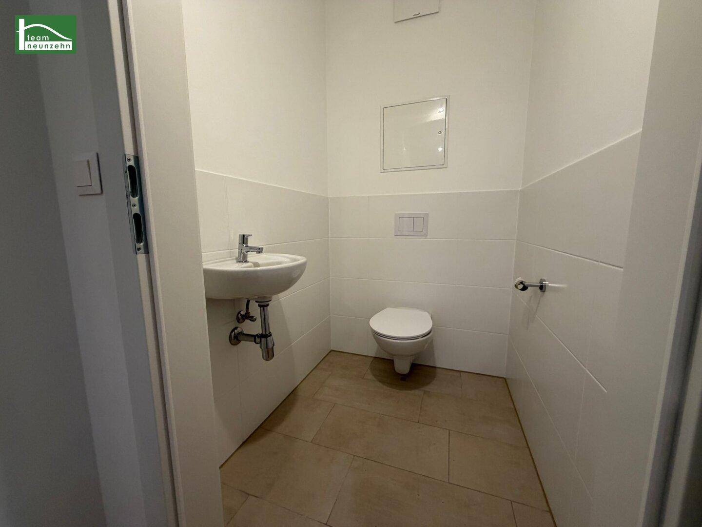 Gäste-WC mit weißen Fliesen, kleinem Waschbecken und wandhängender Toilette.