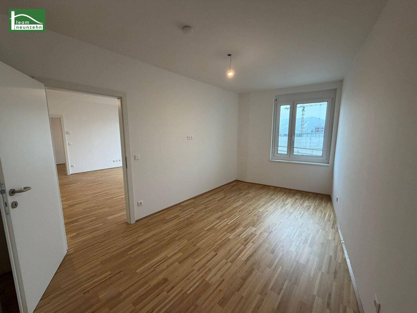 Helles Schlafzimmer mit Parkettboden und großem Fenster, bereit zur Einrichtung.