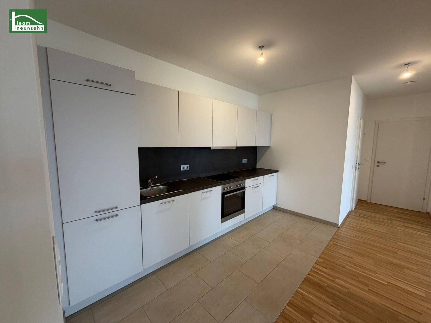 Moderne Einbauküche mit weißen Schränken, dunkler Arbeitsplatte und Fliesenboden.