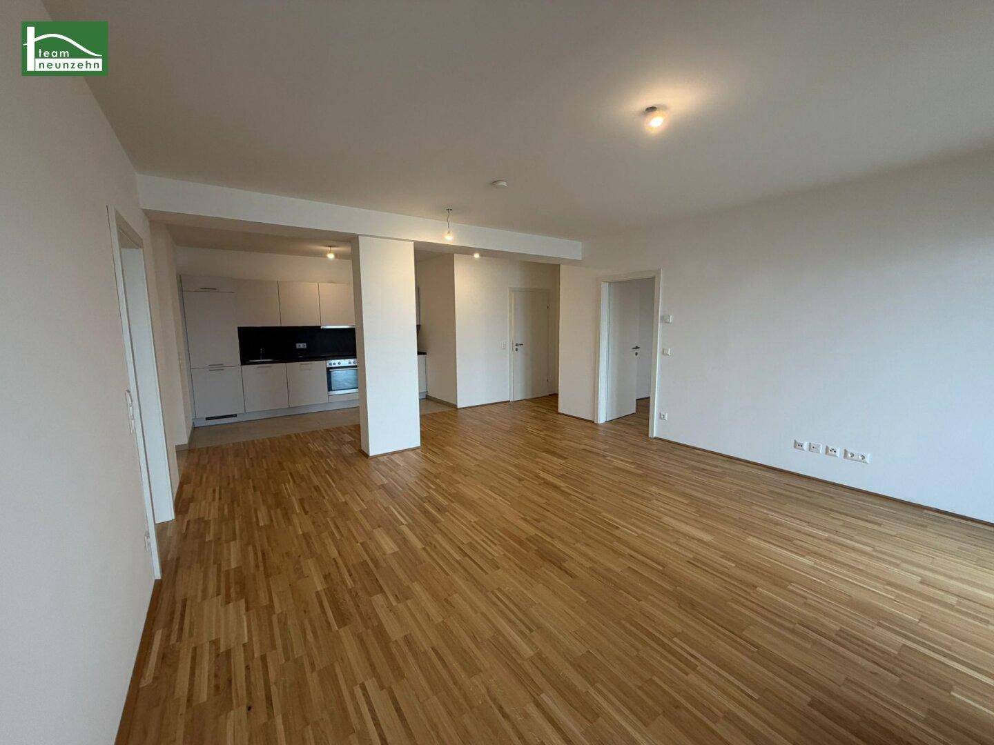 Geräumiges Wohnzimmer mit Parkettboden und Blick auf den Küchenbereich.