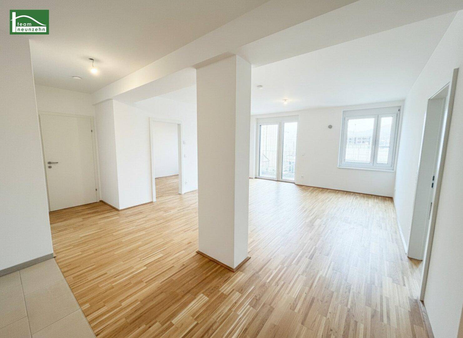 Helles, leeres Wohnzimmer mit Parkettboden und Zugang zu einem Balkon.