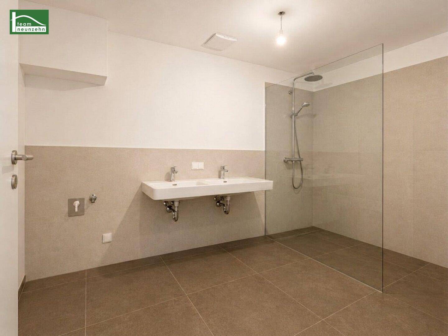 Leeres Badezimmer mit vorbereiteten Anschlüssen für Doppelwaschbecken und begehbarer Dusche.