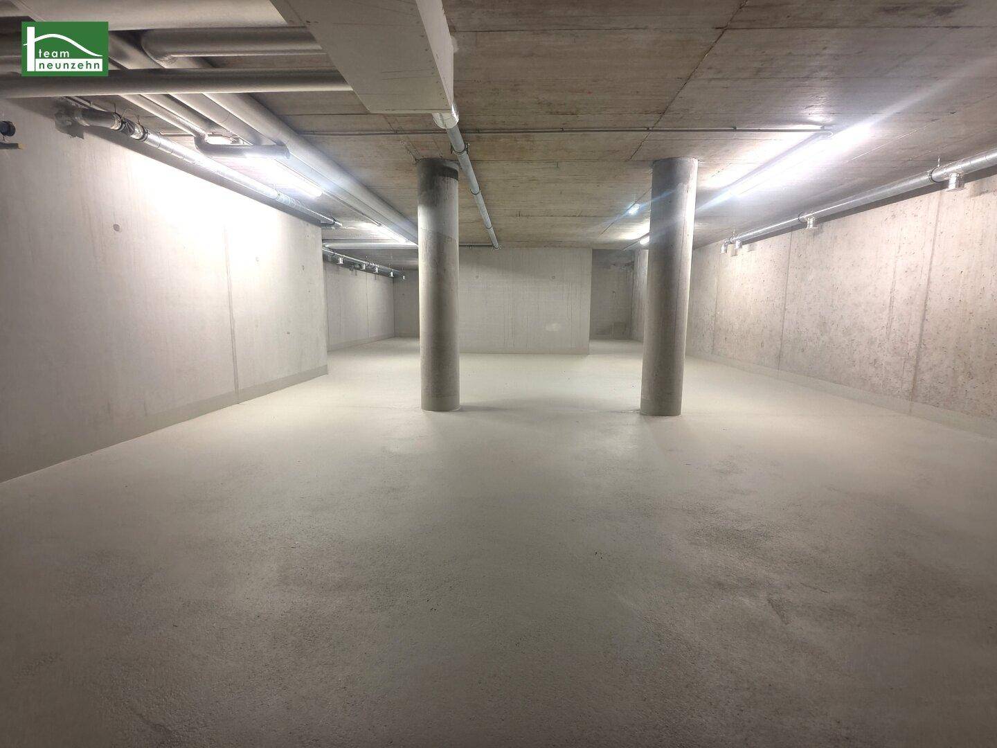 Weitläufiger Blick in einen unfertigen Beton-Keller mit mehreren Stützsäulen und Deckenrohren.